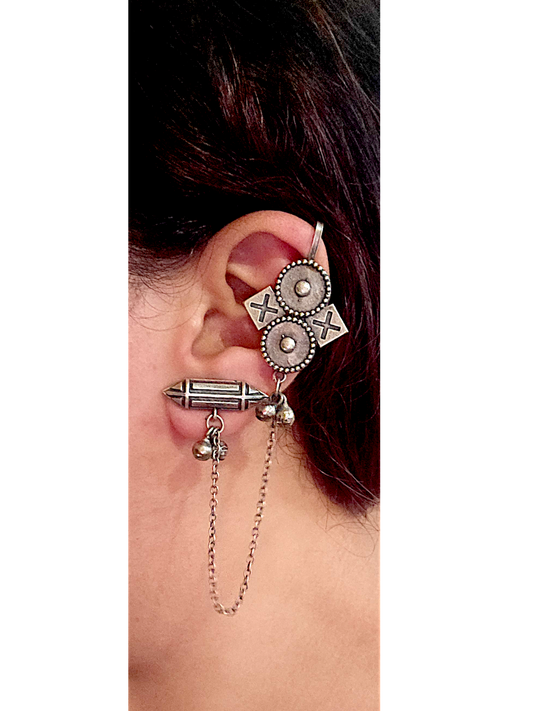Close-up of an ear with a silver ear cuff and dangling earrings on a white background