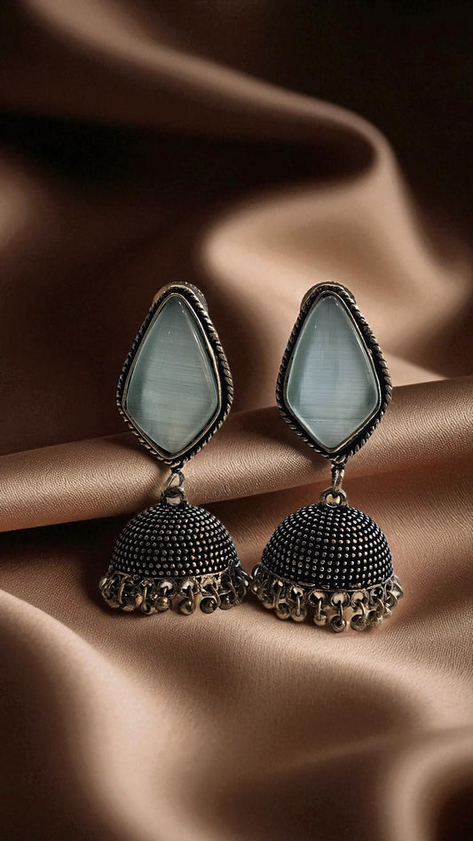 Pair of earrings with teardrop-shaped green stones on a brown fabric background