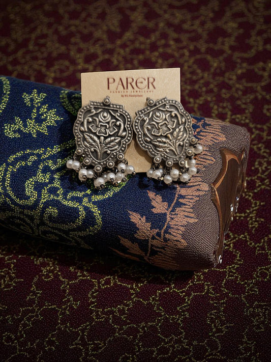 Pair of silver earrings on a decorative cushion with 'Parer' branding.
